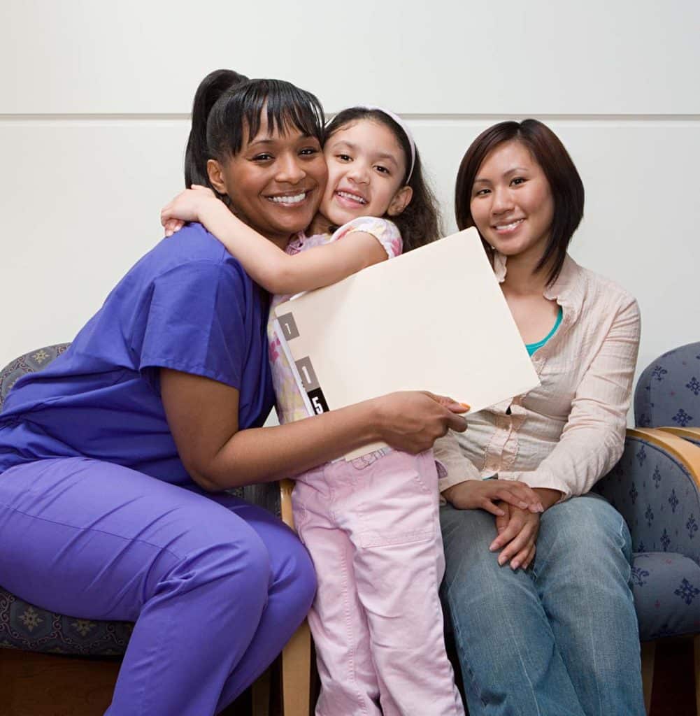 Nurse hugging pediatric patient with mom there too.
